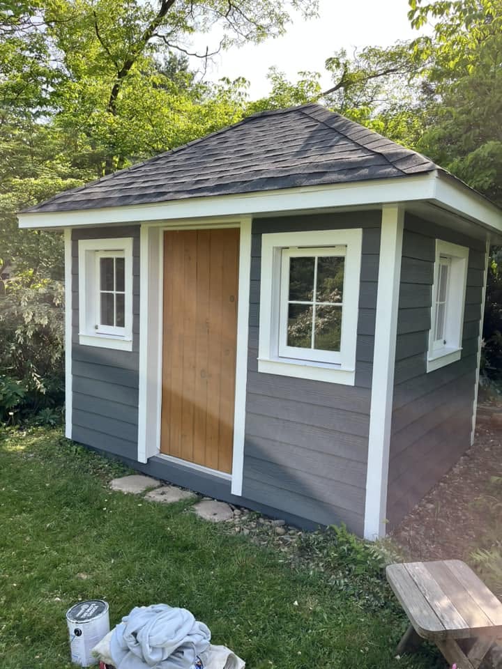 Backyard shed repainted slate gray with crisp white trim and a natural wood door